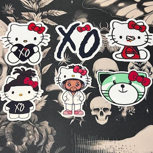 Peut inclure: Un ensemble de six autocollants en vinyle représentant des personnages Hello Kitty avec la marque XO, incluant un personnage tenant un cœur noir, un personnage en costume blanc, un personnage aux cheveux foncés et un chat vert avec un nœud rouge.