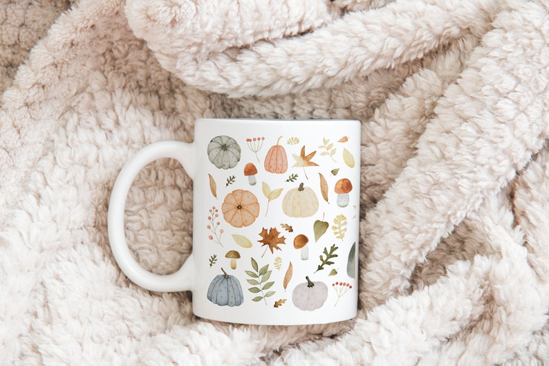 May include: A white ceramic mug with a fall-themed design. The mug features a pattern of pumpkins, leaves, mushrooms, and berries in shades of orange, brown, green, and blue.