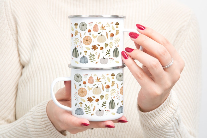 May include: Two white enamel mugs with a fall-themed design featuring pumpkins, leaves, mushrooms, and berries. The mugs are stacked on top of each other.