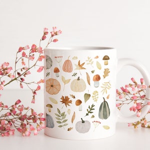 May include: White ceramic mug with a fall-themed design. The mug features a pattern of pumpkins, leaves, mushrooms, and acorns in shades of orange, brown, green, and gray.