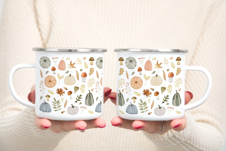 May include: Two white enamel mugs with a fall-themed design. The mugs feature a pattern of pumpkins, leaves, mushrooms, and berries in shades of orange, brown, green, and gray.
