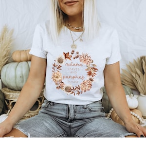 May include: White t-shirt with a floral wreath design and the text "autumn leaves and pumpkins please".