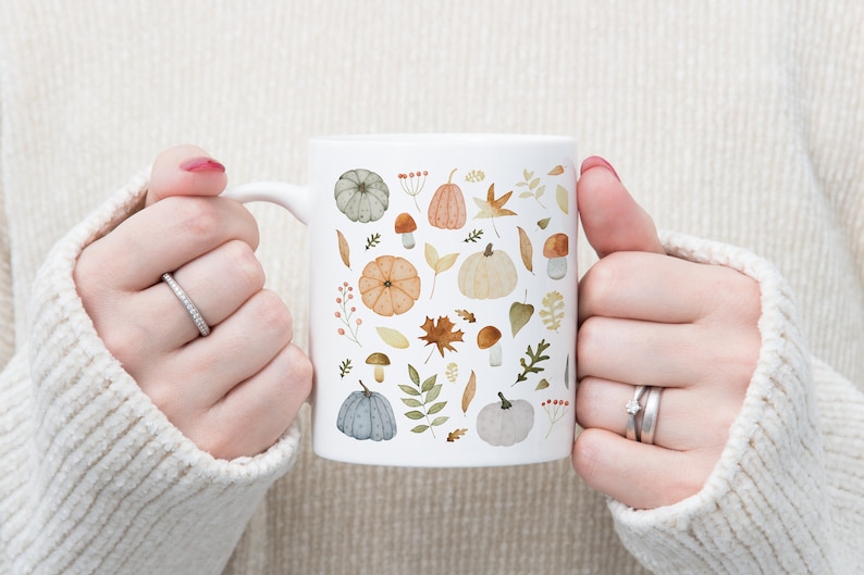 May include: White ceramic mug with a fall-themed design featuring pumpkins, leaves, and mushrooms in shades of orange, brown, green, and gray.