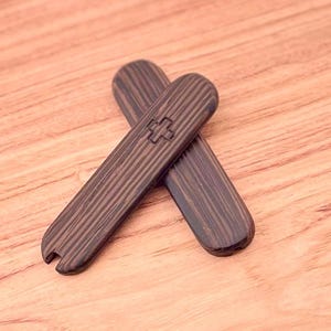 May include: Two wooden tools with a dark brown wood grain finish. The tools are shaped like a rounded rectangle and have a small cross symbol on one side.