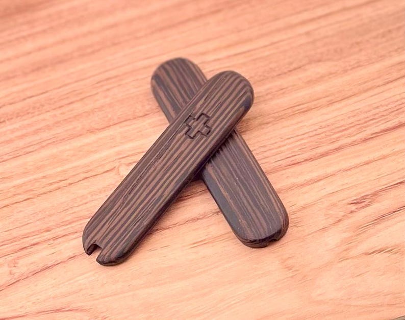 May include: Two wooden tools with a dark brown wood grain finish. The tools are shaped like a rounded rectangle and have a small cross symbol on one side.