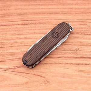 May include: A brown wood-handled pocket knife with a silver blade and a red Swiss cross on the handle.