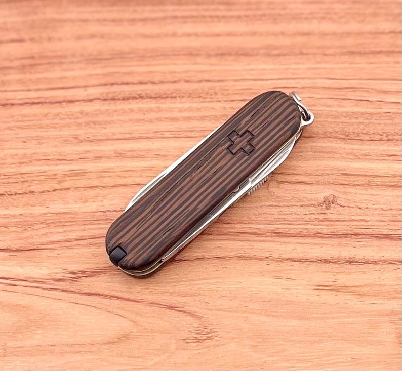 May include: A brown wood-handled pocket knife with a silver blade and a red Swiss cross on the handle.
