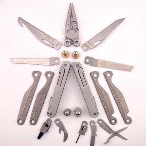 May include: A silver multi-tool with a variety of attachments, including pliers, a saw, a knife, a screwdriver, and a bottle opener. The tools are laid out in a symmetrical pattern on a white background.