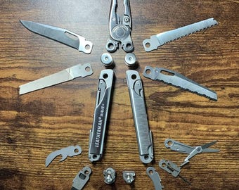 以下が含まれることがあります： ハンドルに「Leatherman Wave+」の文字が刻まれた銀色のマルチツール。ツールが開いており、木製の表面に置かれ、すべてのツールとアタッチメントが周囲に広がっています。