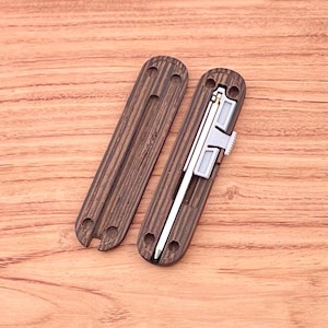 May include: Two wooden cases with a dark brown wood grain pattern. One case is open and reveals a silver metal tool with a gold accent. The tool is a pen or a small knife.