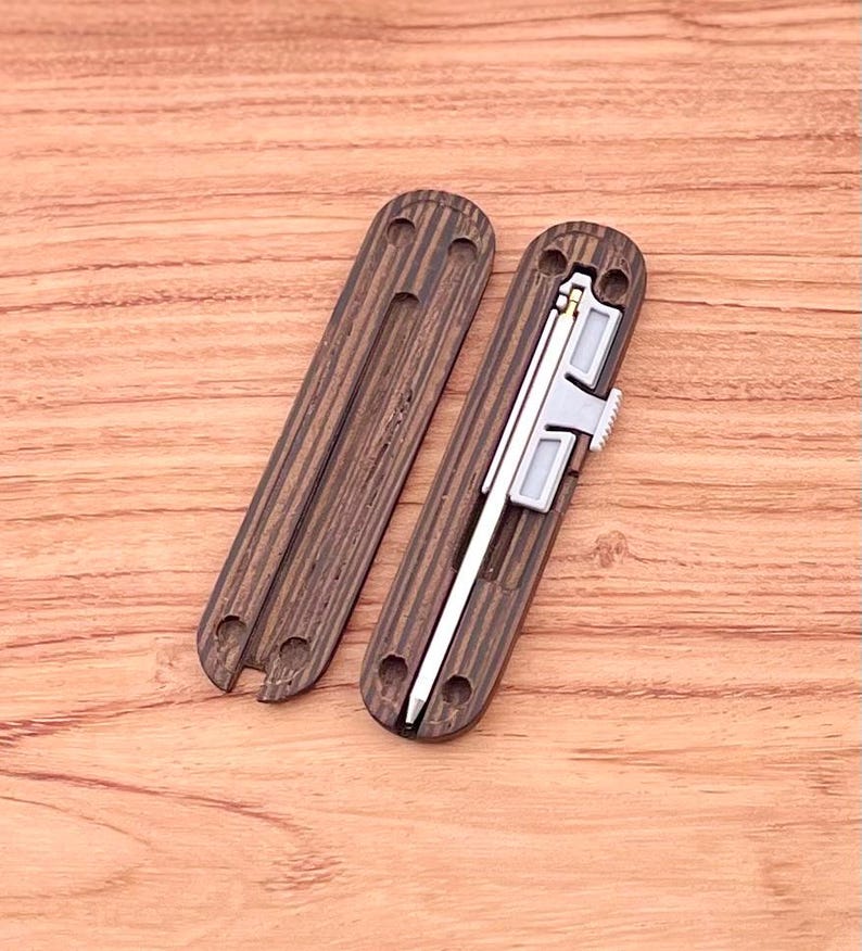 May include: Two wooden cases with a dark brown wood grain pattern. One case is open and reveals a silver metal tool with a gold accent. The tool is a pen or a small knife.