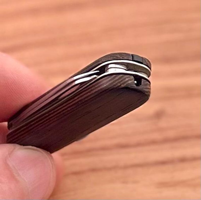 May include: A black pocket knife with a wood grain pattern and a silver blade. The knife is closed and the blade is visible.