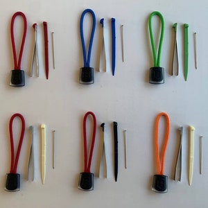 May include: Six sets of colourful zipper pulls with a small black tool and a needle. Each set includes a red, blue, green, orange, red, and red zipper pull.