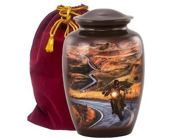 May include: A brown ceramic urn with a scenic image of a motorcycle on a winding road. The urn has a lid and comes with a burgundy velvet bag.