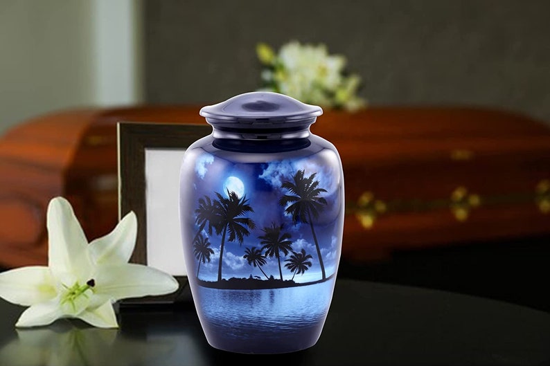 Puede incluir: Una urna de cremaci&oacute;n azul y plateada con una escena tropical de palmeras y una luna llena reflejada en el agua.