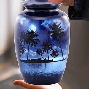 Puede incluir: Una urna de cer&aacute;mica azul con una silueta de palmeras y una luna llena sobre un fondo de cielo y agua azules.