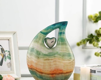 May include: A green, orange, and white abstract heart-shaped ceramic sculpture with a silver heart inside. The sculpture is on a white surface.