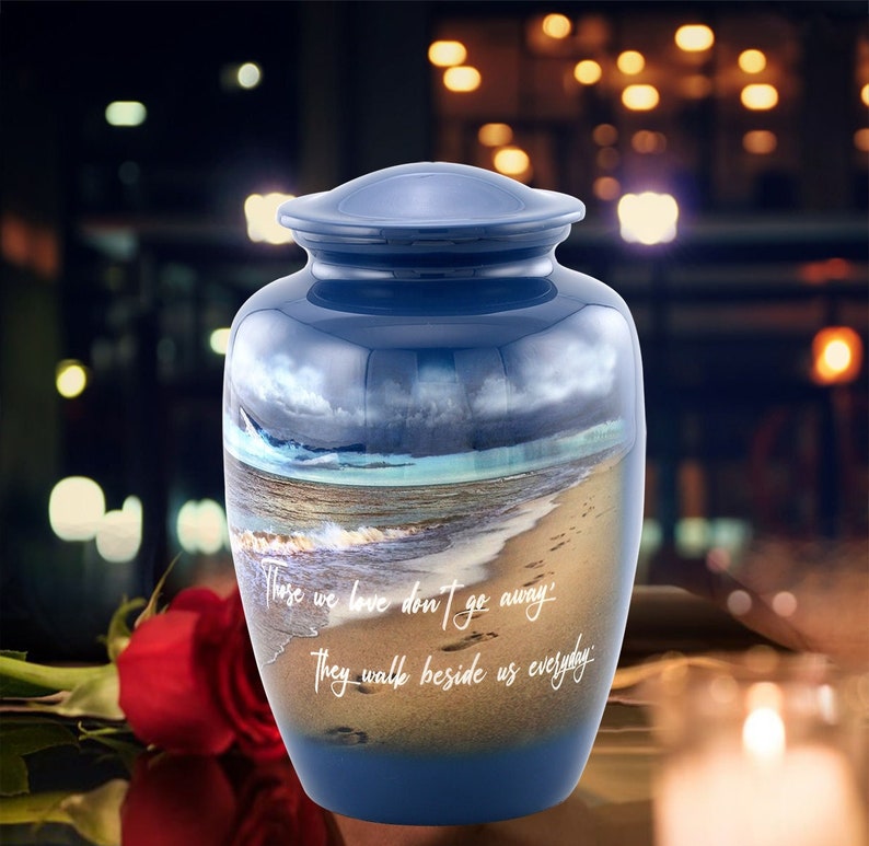 May include: Blue ceramic cremation urn with a beach scene and the quote "Those we love don't go away, they walk beside us everyday".
