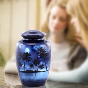 Puede incluir: Una urna de cer&aacute;mica azul con un dise&ntilde;o de luna blanca y palmeras. La urna est&aacute; decorada con una escena de playa tropical nocturna.