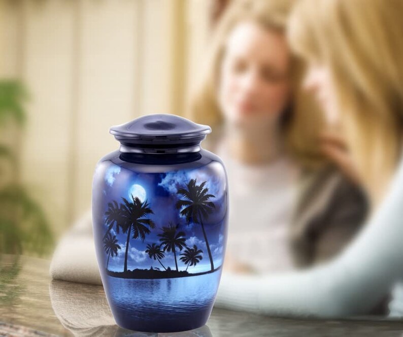 Puede incluir: Una urna de cer&aacute;mica azul con un dise&ntilde;o de luna blanca y palmeras. La urna est&aacute; decorada con una escena de playa tropical nocturna.