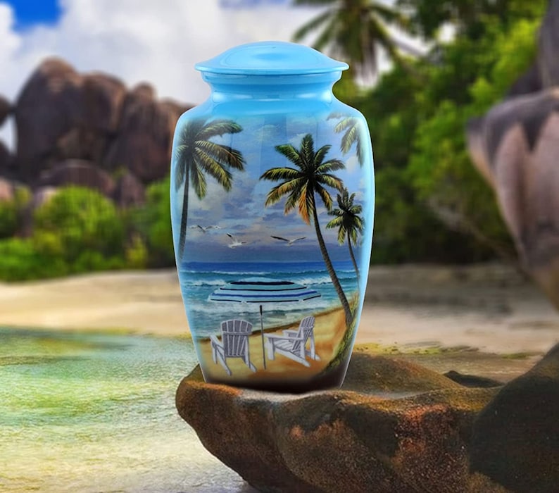 May include: A blue ceramic urn with a beach scene painted on it. The scene includes palm trees, an ocean, a beach, and two chairs with an umbrella.