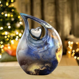 May include: A blue and gold ceramic urn with a heart-shaped opening. The urn has a swirling, cloudy design and a silver heart inside the opening.