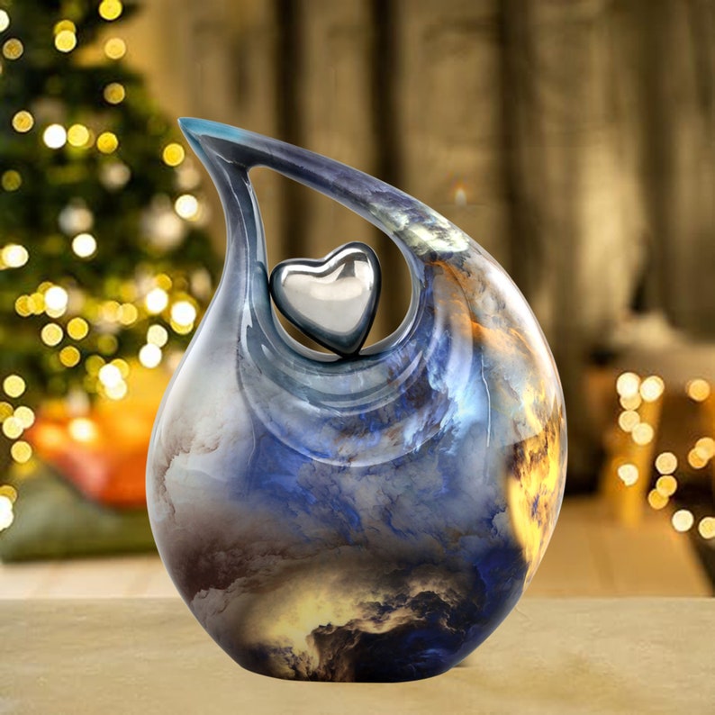 May include: A blue and gold ceramic urn with a heart-shaped opening. The urn has a swirling, cloudy design and a silver heart inside the opening.