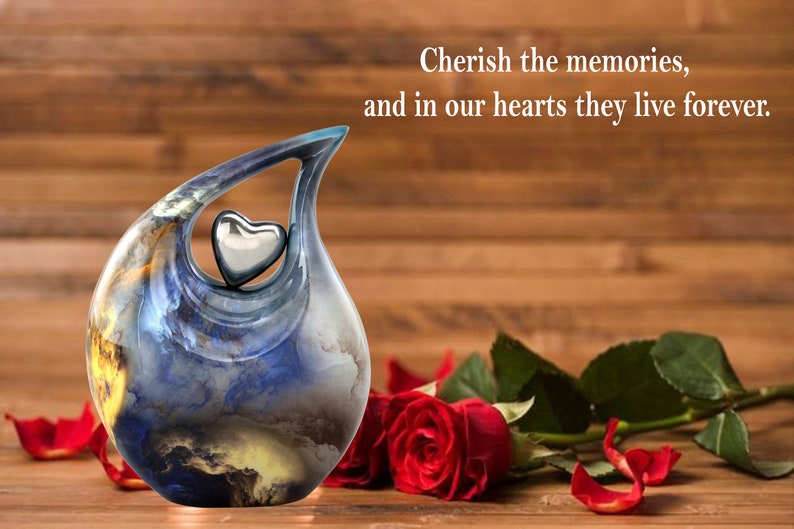 May include: A blue and gold ceramic urn with a silver heart on top. The urn is sitting on a wooden surface with red roses and petals.