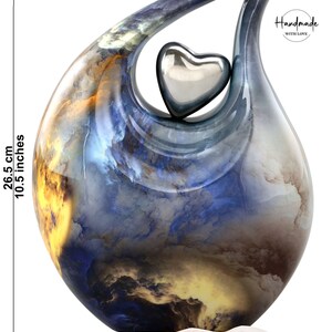 May include: A blue and yellow ceramic urn shaped like a teardrop with a silver heart on top. The urn is 10.5 inches tall and 8 inches wide. It is designed to hold human ashes up to 210 cubic inches. The urn is handmade with love and says "Silent Goodbyes, Memories are Forever".