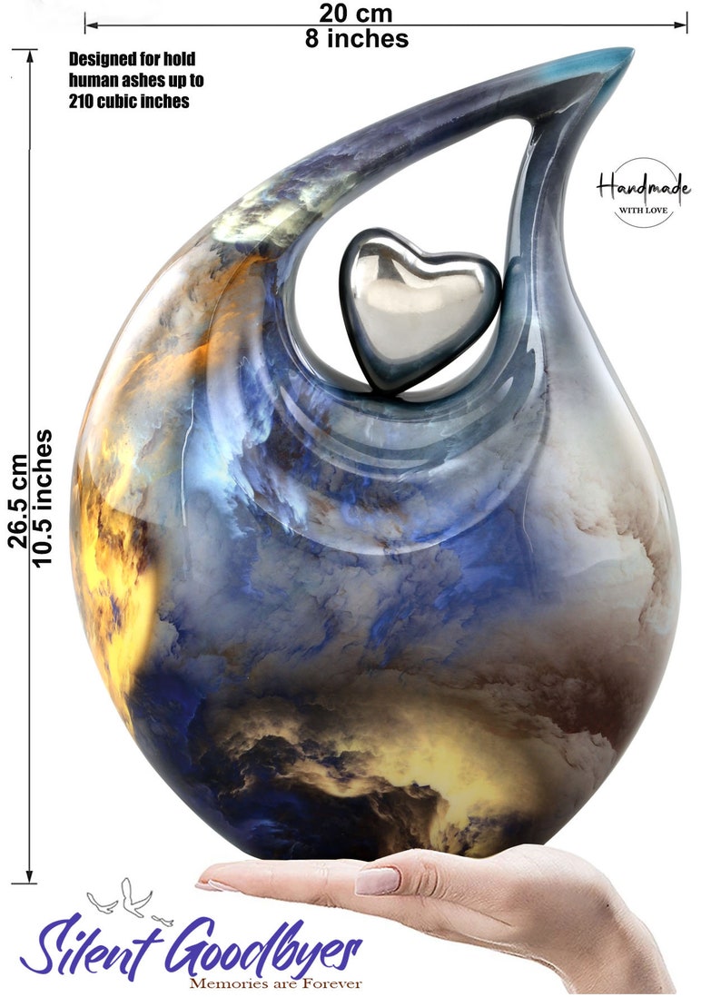 May include: A blue and yellow ceramic urn shaped like a teardrop with a silver heart on top. The urn is 10.5 inches tall and 8 inches wide. It is designed to hold human ashes up to 210 cubic inches. The urn is handmade with love and says "Silent Goodbyes, Memories are Forever".