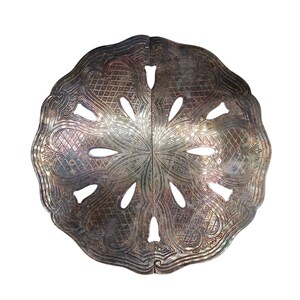 Pode incluir: Um descanso de panela circular em metal prateado com um padrão simétrico em relevo, design de treliça e bordas recortadas. O objeto é composto por duas metades idênticas unidas, com oito recortes em formato de gota.