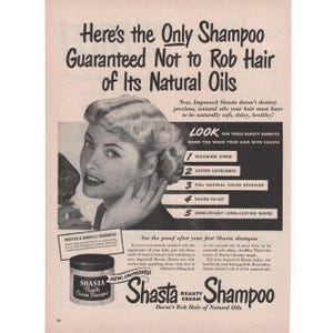 Puede incluir: Anuncio vintage de Shasta Beauty Cream Shampoo. El anuncio en blanco y negro presenta a una mujer con el pelo peinado y un tarro del champú. El texto destaca beneficios como brillo y suavidad.