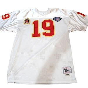 Pode incluir: Camisola de malha branca com o número 19 vermelho e acabamento dourado. A camisola tem números vermelhos nas mangas e patches no peito. É um estilo retro de 1994.