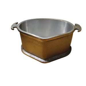 Puede incluir: Una olla cuadrada de hierro fundido con exterior bronce y interior plateado. La olla tiene dos asas y una base redondeada. La olla está vacía y lista para usar.