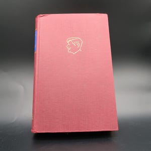 May include: A red hardcover book with a gold illustration of a man's head on the front cover.