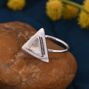 Puede incluir: Un anillo de plata con un engaste de forma triangular. El anillo est&aacute; sobre una roca marr&oacute;n.
