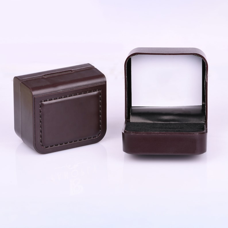 Puede incluir: Dos cajas de anillos de imitaci&oacute;n de cuero marr&oacute;n. Una caja est&aacute; cerrada y la otra est&aacute; abierta, mostrando un interior de terciopelo negro.