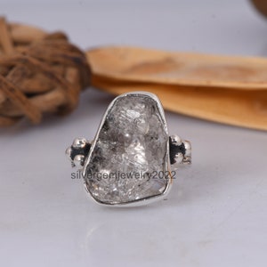 May include: A silver ring with a large, rough, clear quartz stone set in the center. The band is decorated with small silver beads.