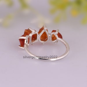 May include: A silver ring with five orange gemstones set in a row. The ring is shown from the side, with the gemstones facing the viewer.
