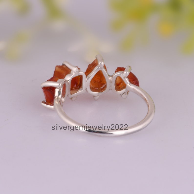 May include: A silver ring with five orange gemstones set in a row. The ring is shown from the side, with the gemstones facing the viewer.