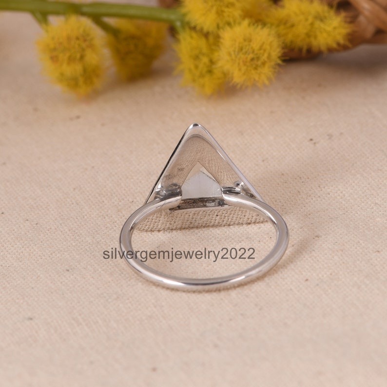 Puede incluir: Anillo de plata de forma triangular con un acabado liso y pulido. El anillo se muestra desde la parte posterior, mostrando la forma triangular y la banda lisa.