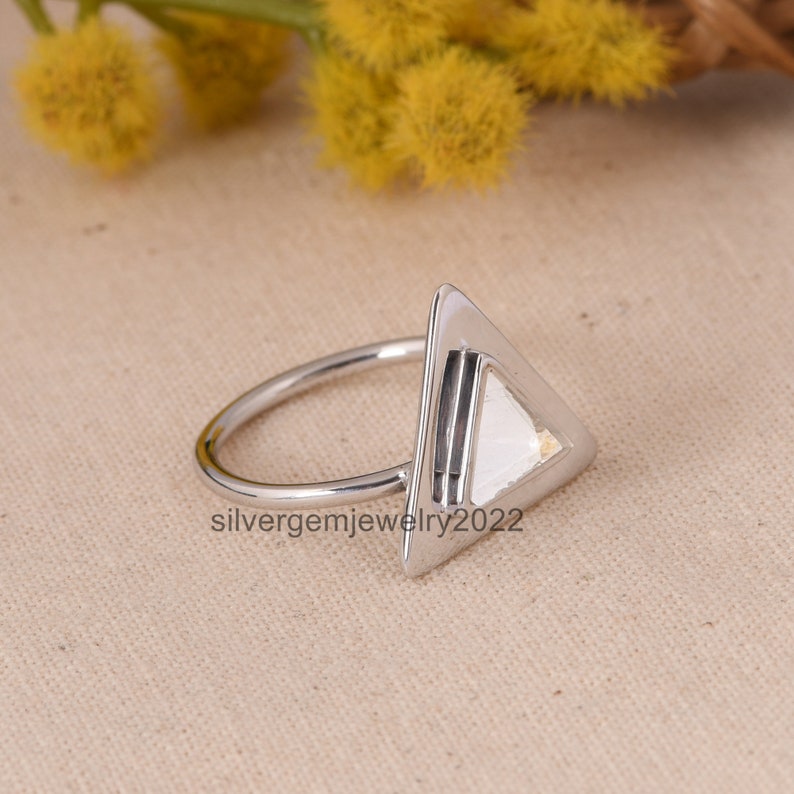 Puede incluir: Un anillo de plata en forma de tri&aacute;ngulo con un dise&ntilde;o geom&eacute;trico. El anillo est&aacute; hecho de plata de ley y tiene un acabado pulido.