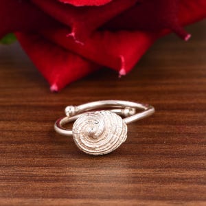 May include: A silver ring with a spiral shell design. The ring is on a wooden surface.