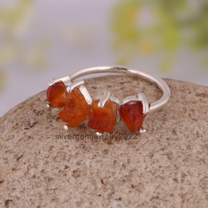May include: Silver ring with five orange carnelian stones set in a row. The stones are raw and have a natural, irregular shape.