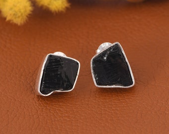 May include: A pair of silver earrings with black gemstone studs. The gemstones are irregularly shaped and have a rough, natural look.