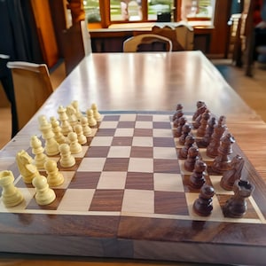 K&ouml;nnte beinhalten: Ein Schachspiel aus Holz mit hell- und dunkelbraunen Feldern und Figuren. Die Schachfiguren sind auf dem Brett angeordnet und bereit f&uuml;r ein Spiel. Die hellen Figuren sind elfenbeinfarben und die dunklen Figuren sind braun.