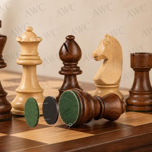 K&ouml;nnte beinhalten: Ein Schachspiel aus Holz mit Figuren in verschiedenen Braun- und Beiget&ouml;nen. Die Figuren umfassen einen K&ouml;nig, eine Dame, einen L&auml;ufer, einen Springer, einen Turm und einen Bauern, angeordnet auf einem karierten Holzbrett. Der K&ouml;nig ist dunkelbraun, und die Dame ist hellbeige.