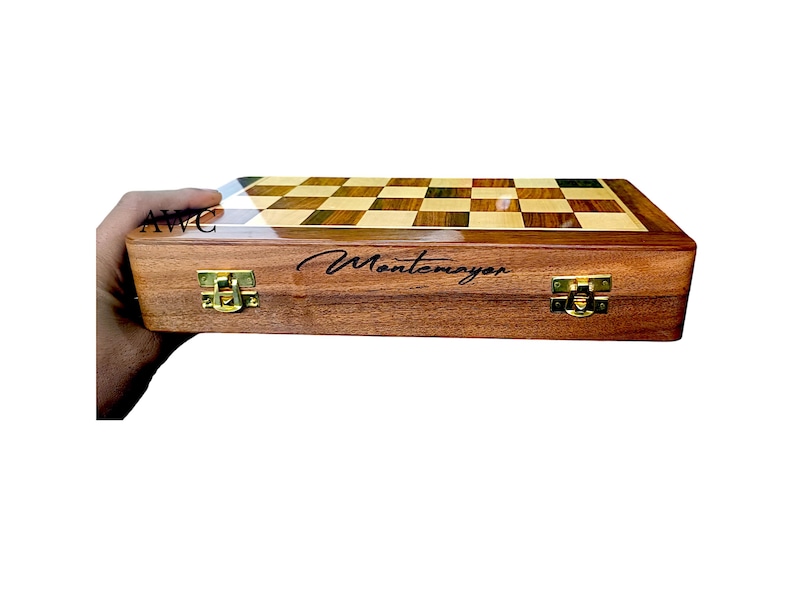 K&ouml;nnte beinhalten: Ein Schachspiel aus Holz mit einem Schachbrettmuster in hellen und dunklen Holzt&ouml;nen. Die Box ist braun mit goldfarbenen Verschl&uuml;ssen und der Name "Montemayor" ist auf der Vorderseite geschrieben.