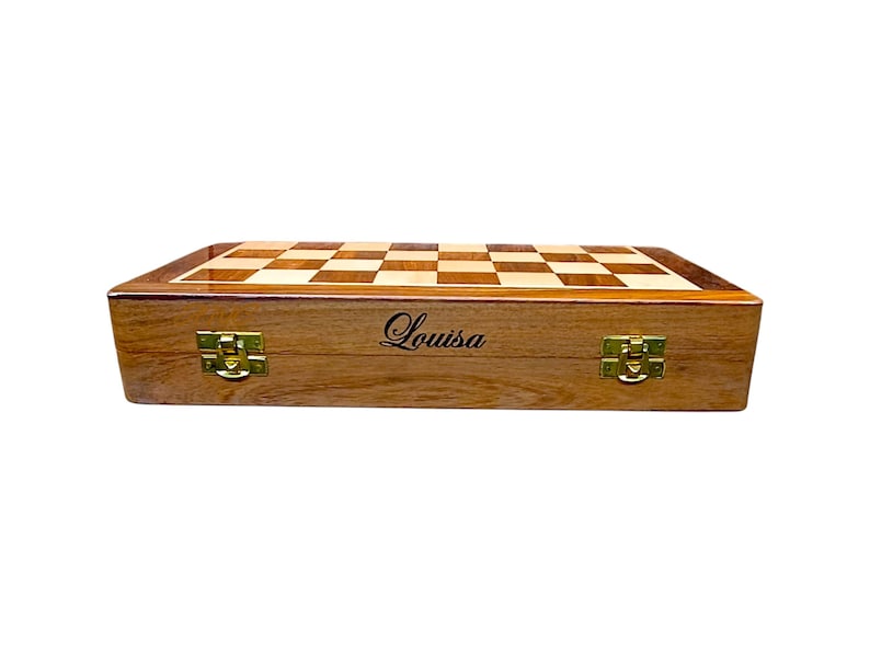 K&ouml;nnte beinhalten: Ein Schachspiel aus Holz mit einem hellen und dunklen Schachbrett. Die Holzbox hat goldfarbene Verschl&uuml;sse und der Name "Louisa" ist auf der Vorderseite geschrieben. Das Schachspiel ist geschlossen und bereit f&uuml;r die Aufbewahrung oder den Transport.