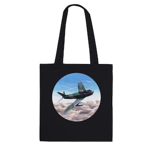 May include: Black tote bag with a circular design featuring a green and gray airplane flying in a blue sky with white clouds. The airplane has a German flag on the tail.